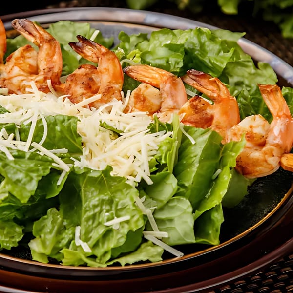 A close-up of a fresh green salad topped with grilled shrimp and shredded cheese.