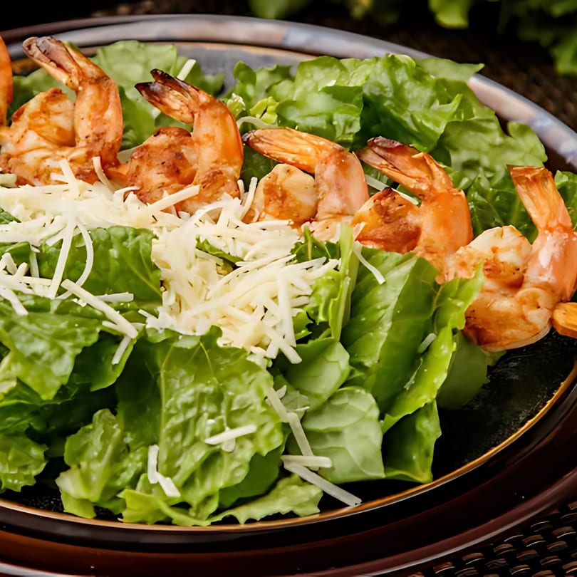 A close-up of a fresh green salad topped with grilled shrimp and shredded cheese.