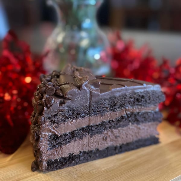 A slice of rich chocolate cake with multiple layers of frosting and chocolate chips on top.