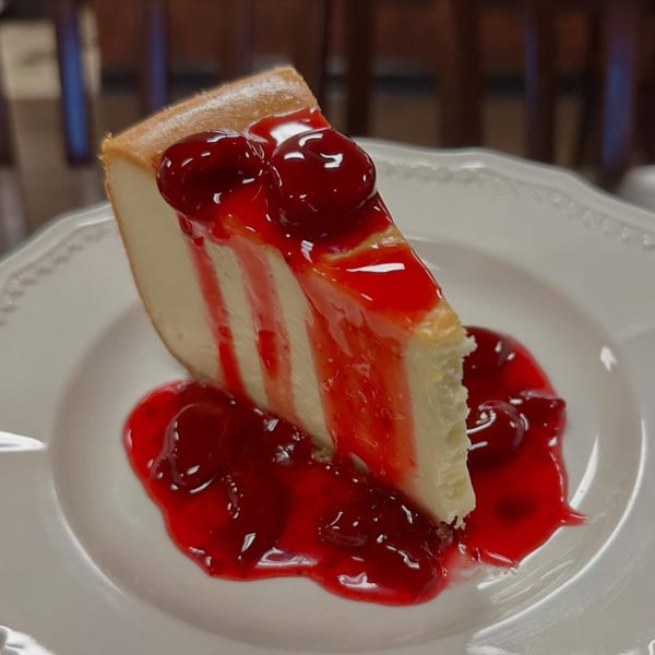 Slice of Steak-Out's cheesecake with cherry topping and sauce on a white plate.