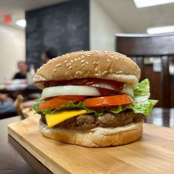A Steak-Out cheeseburger with lettuce, tomato, onion, and ketchup on a wooden board.